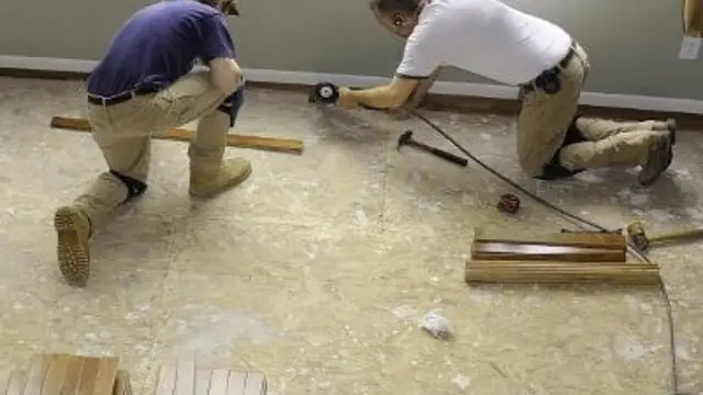 Two workers kneeling to remove damaged flooring down to the subfloor